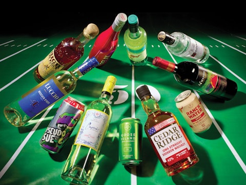 A spread of a tailgating drinks story from Hy-Vee Mega Ad magazine, featuring various bottles and cans huddling up on a football field.
