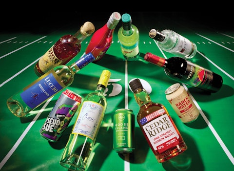A spread of a tailgating drinks story from Hy-Vee Mega Ad magazine, featuring various bottles and cans huddling up on a football field.