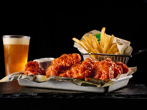 A tray of hot wings, basket of fries, and a cold beer from Wahlburgers.