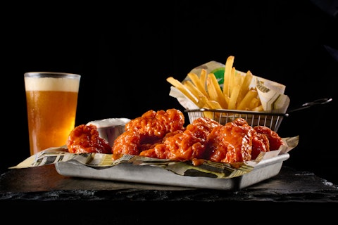 A tray of hot wings, basket of fries, and a cold beer from Wahlburgers.